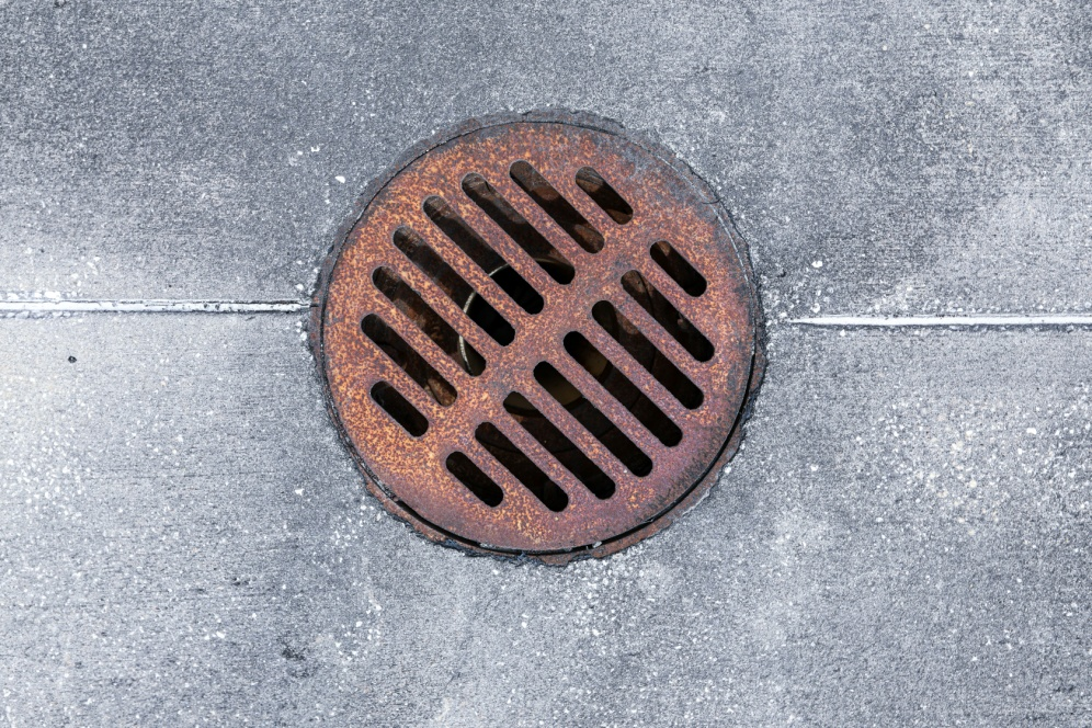 Rusted metal storm drain grate embedded in concrete surface