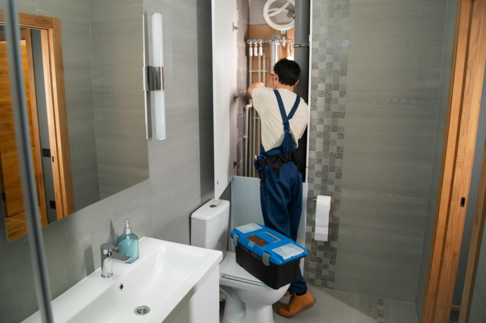 Plumber inspecting and repairing exposed bathroom plumbing lines inside a residential property