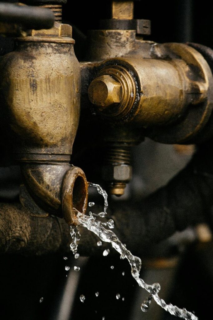 Water leaking from worn metal pipe connection with visible corrosion