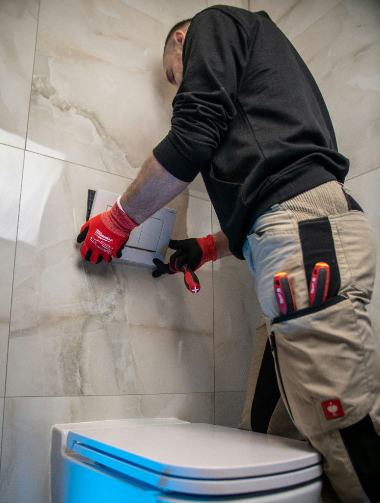 Technician performing repair work on a wall-mounted toilet fixture